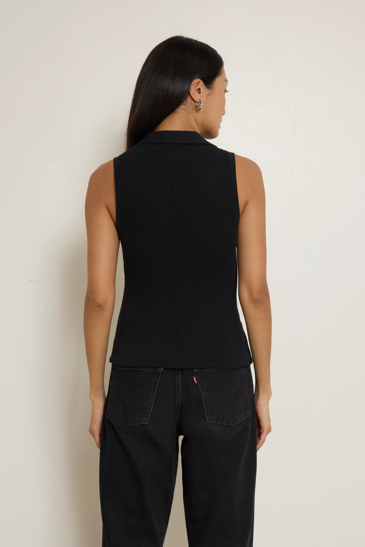 Person wearing a black sleeveless top and black pants against a plain background
