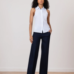 Woman wearing a white sleeveless blouse and navy pants on a plain background