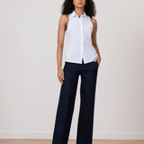 Woman wearing a white sleeveless blouse and navy pants on a plain background