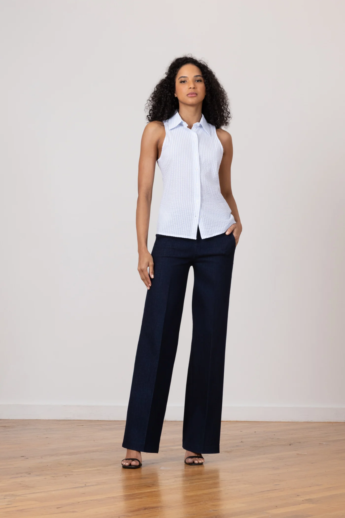 Woman wearing a white sleeveless blouse and navy pants on a plain background