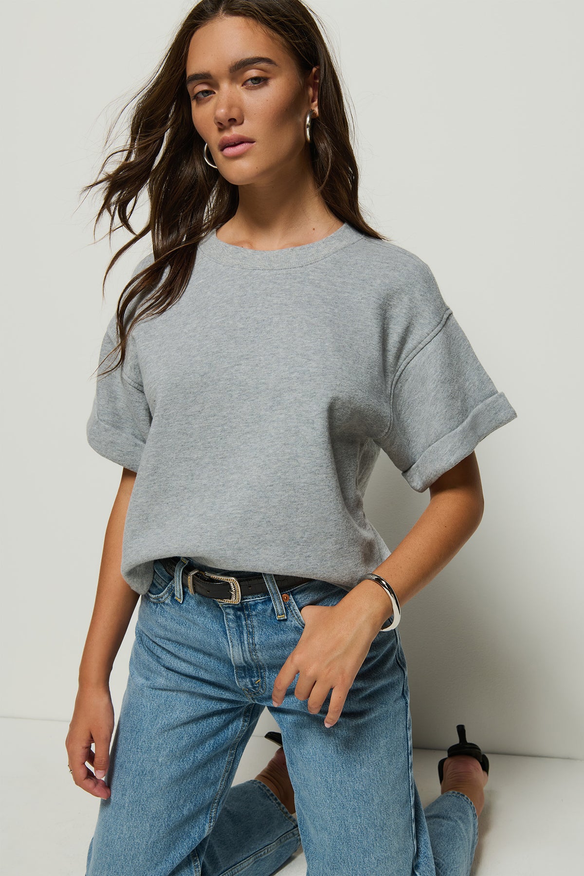 Woman wearing a gray oversized t-shirt and blue jeans against a white background