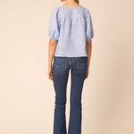 back of woman in blue top and denim on tan background 