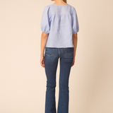 back of woman in blue top and denim on tan background 