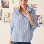 Woman wearing a blue striped shirt in an office setting with bulletin board in the background