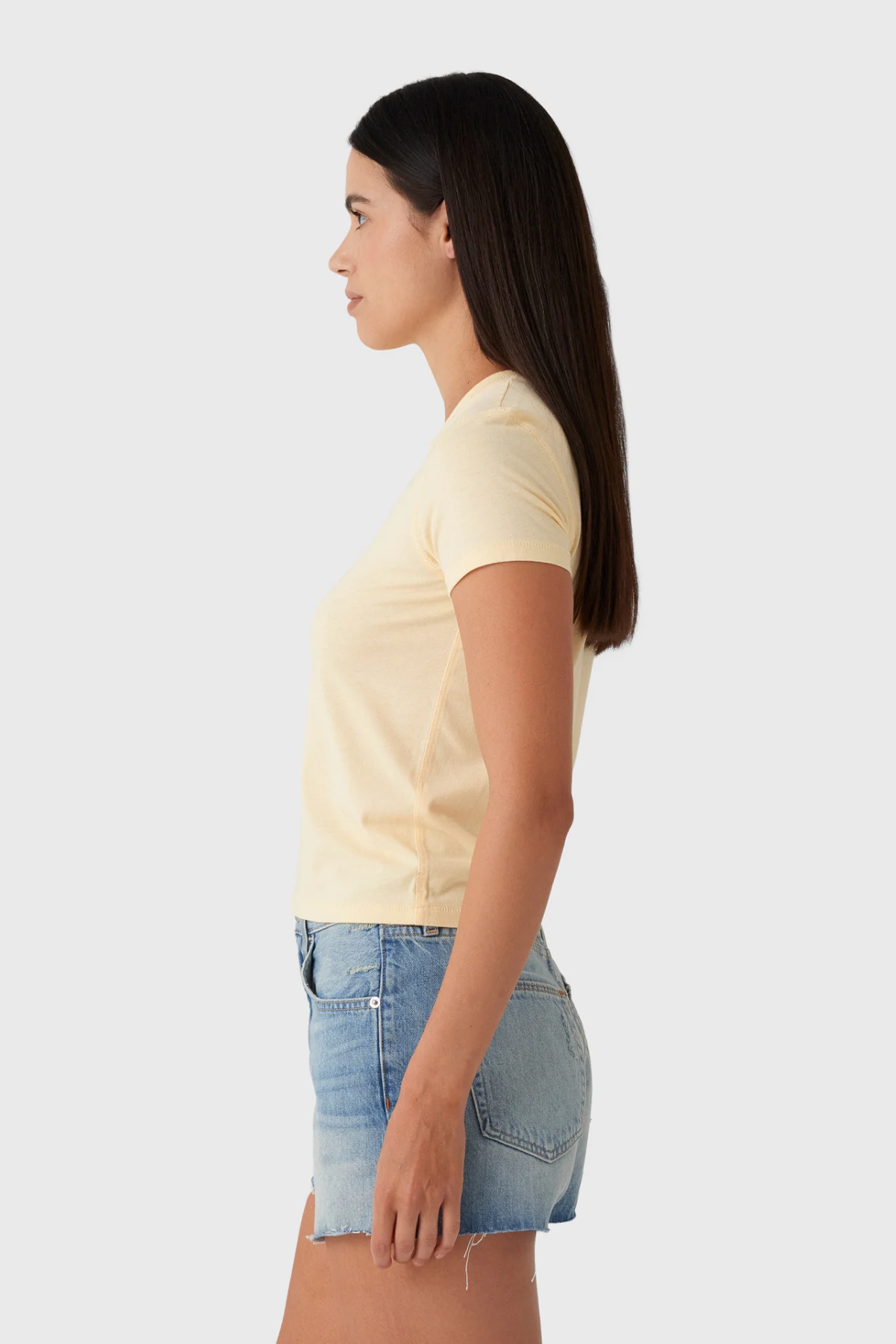 Woman wearing a light yellow t-shirt and denim shorts on a white background