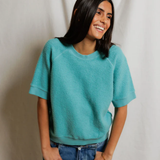 Person wearing a teal sweater and blue jeans against a plain background