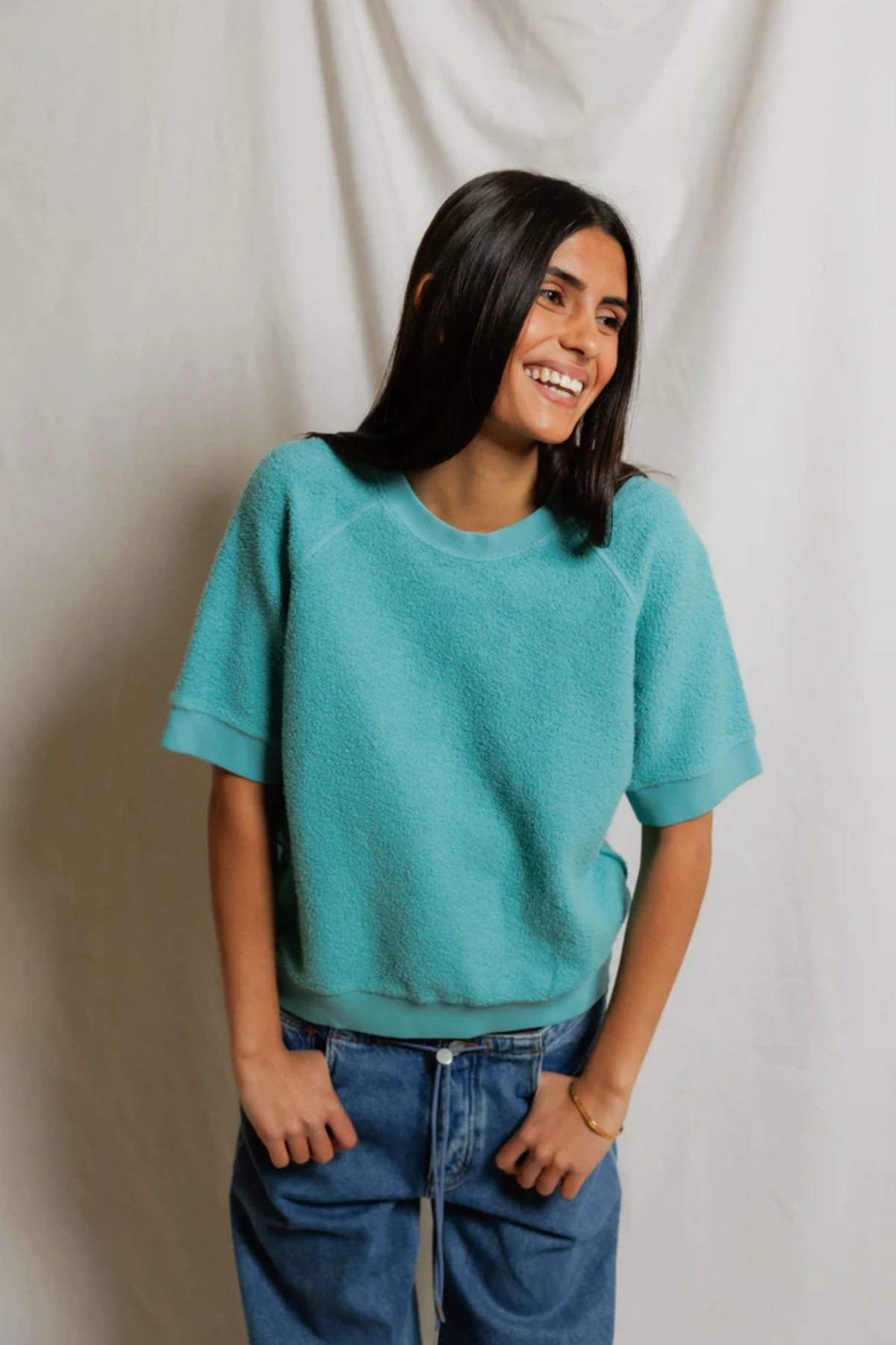 Person wearing a teal sweater and blue jeans against a plain background