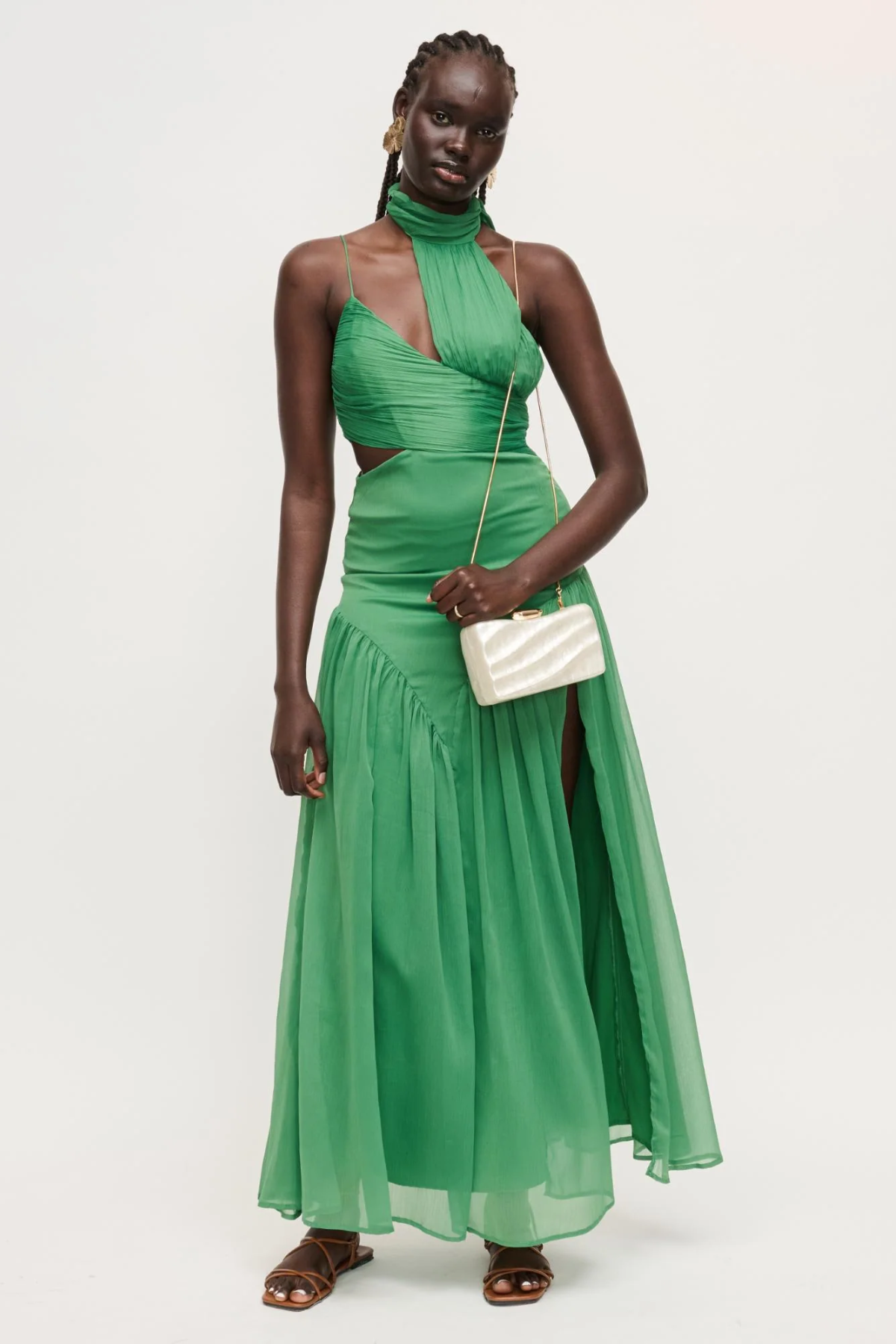 Woman wearing a green evening gown with a white clutch against a light gray background