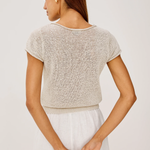 Woman wearing a beige knit top and white shorts on a plain background