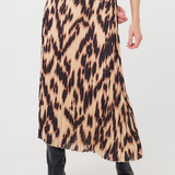 A model wearing a pleated midi skirt with a brown and beige animal print, paired with a brown ribbed top and black ankle boots, shown from the waist down on a white studio background.