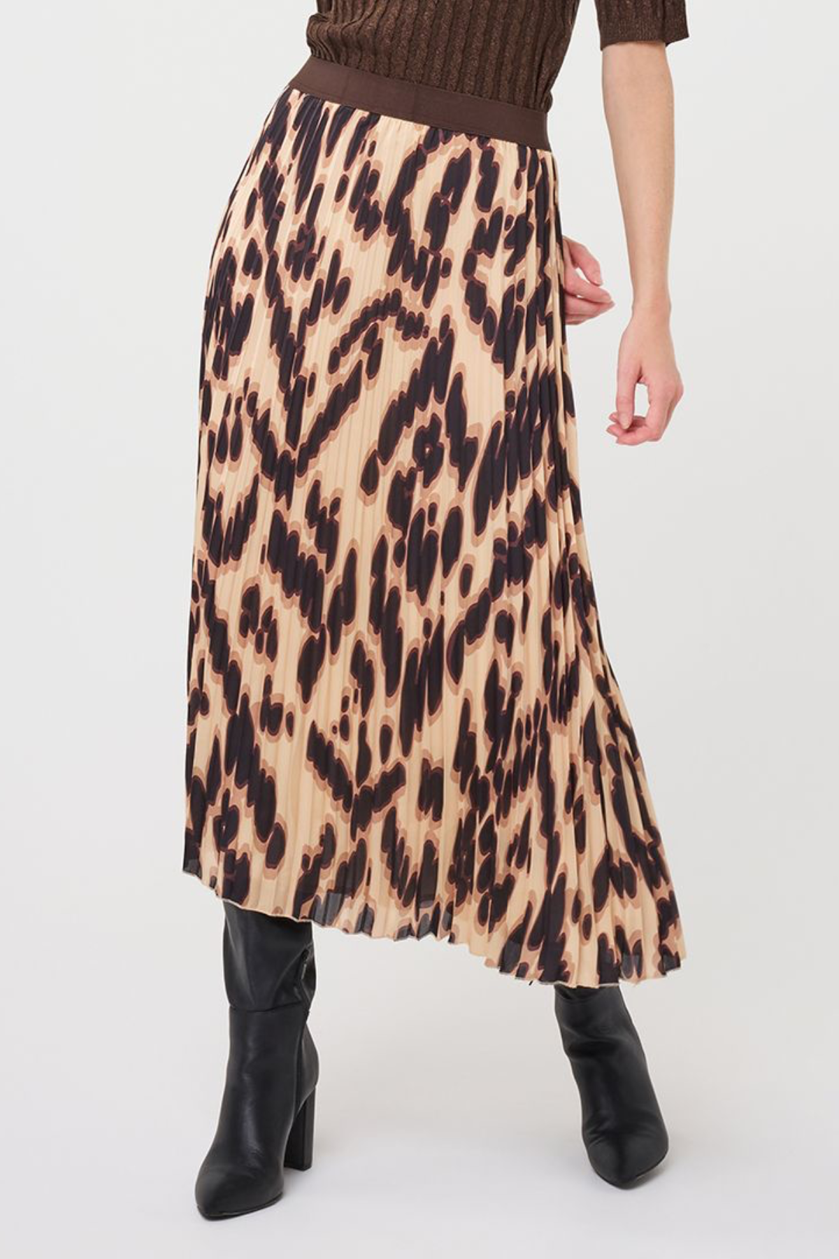 A model wearing a pleated midi skirt with a brown and beige animal print, paired with a brown ribbed top and black ankle boots, shown from the waist down on a white studio background.