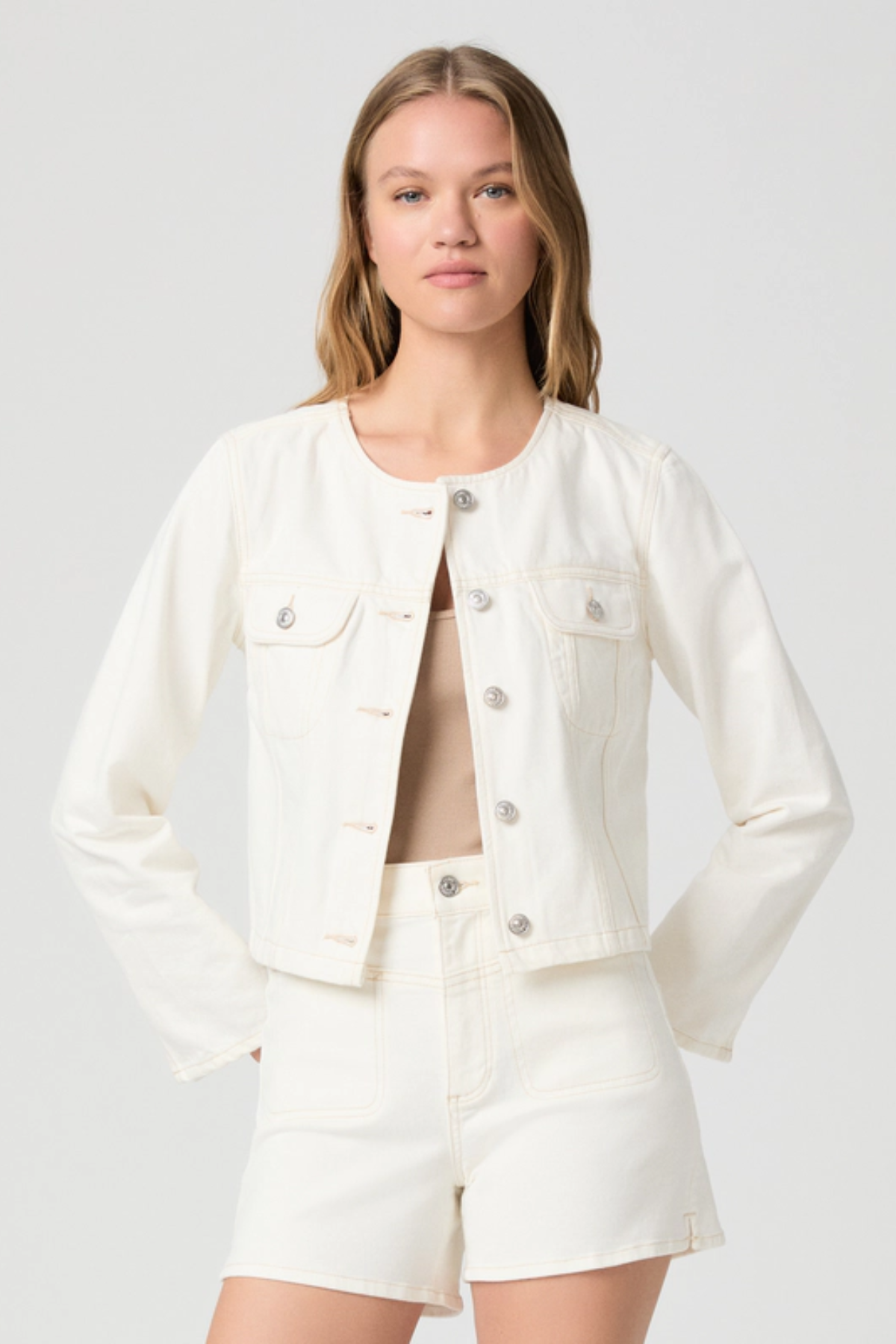 Woman wearing a white denim jacket and shorts on a plain background