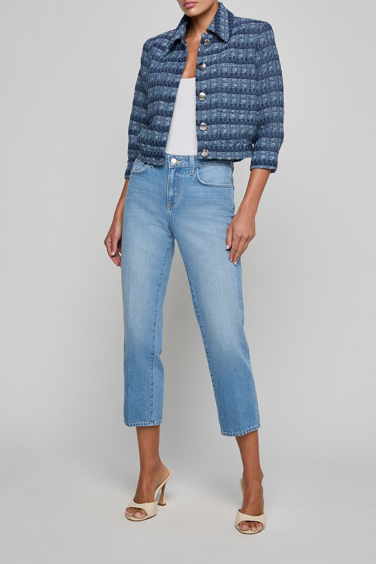 Woman wearing a blue patterned jacket and light blue jeans on a gray background