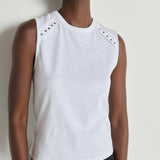 Woman wearing a white sleeveless top with decorative elements on a plain background