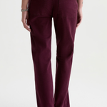 A person shown from the back wearing dark plum-colored straight-leg jeans, a brown long-sleeve top, and brown suede shoes against a plain white studio background.