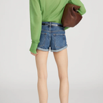 Person wearing a green shirt and denim shorts holding a brown bag on a white background