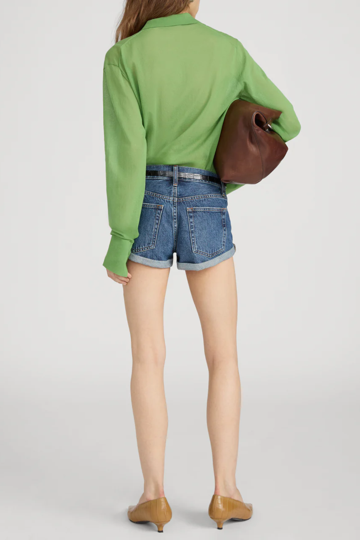 Person wearing a green shirt and denim shorts holding a brown bag on a white background