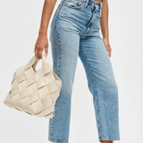 Person wearing light blue jeans and a black top, holding a woven beige bag on a white background