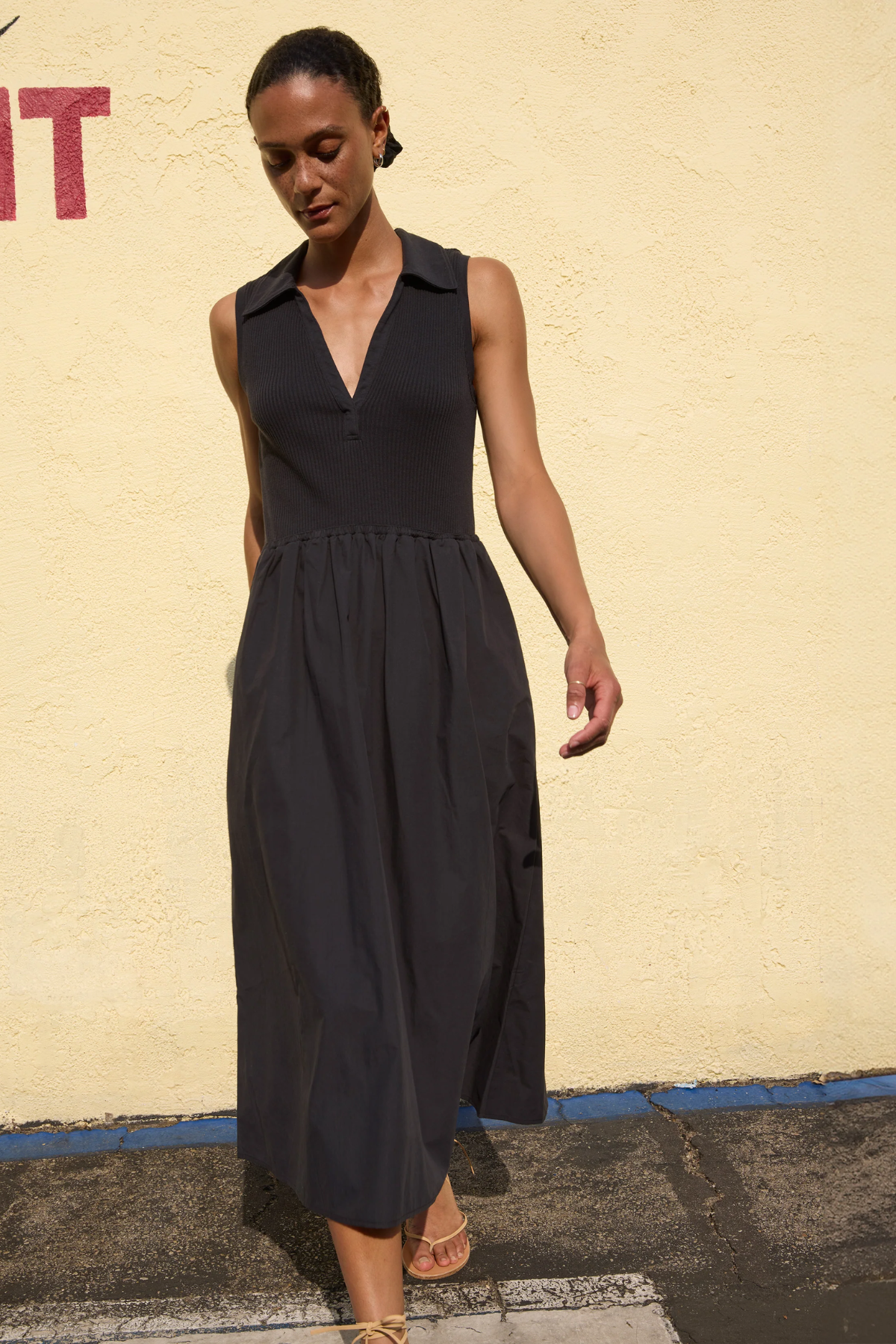 Woman wearing a black sleeveless dress against a beige wall.