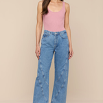 Woman wearing a pink tank top and blue jeans against a beige background
