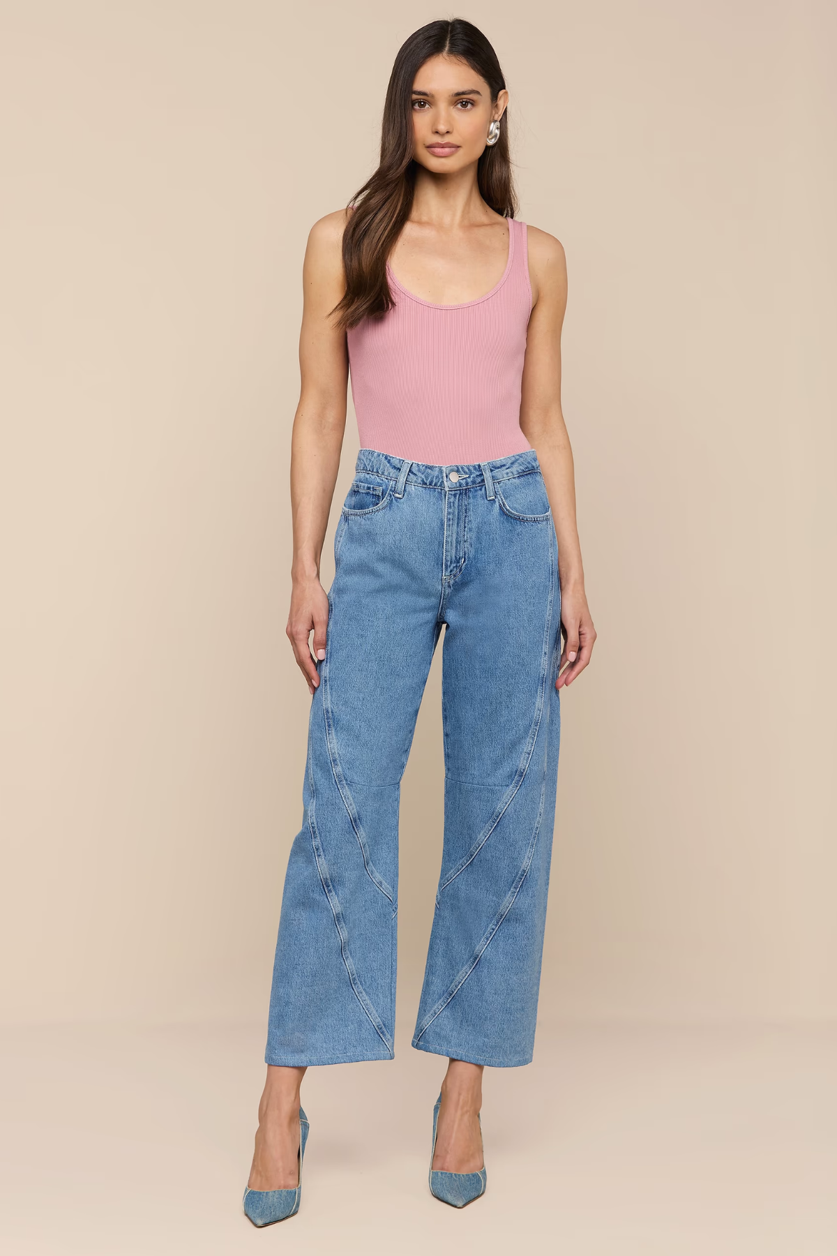 Woman wearing a pink tank top and blue jeans against a beige background