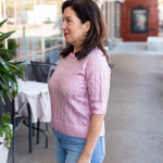 Woman wearing a pink sweater and blue jeans standing outdoors.