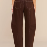 Rear view of a model wearing dark brown wide-leg cropped pants with contrast stitching, paired with a taupe top and dark brown ankle boots, against a solid beige background.