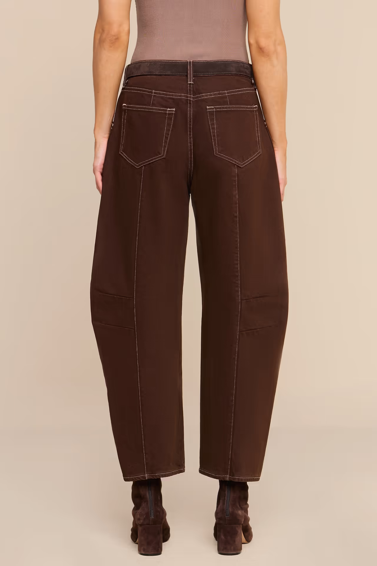 Rear view of a model wearing dark brown wide-leg cropped pants with contrast stitching, paired with a taupe top and dark brown ankle boots, against a solid beige background.