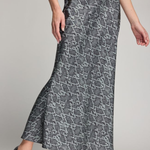 A woman modeling a high-waisted, floor-length skirt with a gray and black snakeskin pattern, paired with black heels, against a neutral studio background.