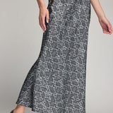 A woman modeling a high-waisted, floor-length skirt with a gray and black snakeskin pattern, paired with black heels, against a neutral studio background.