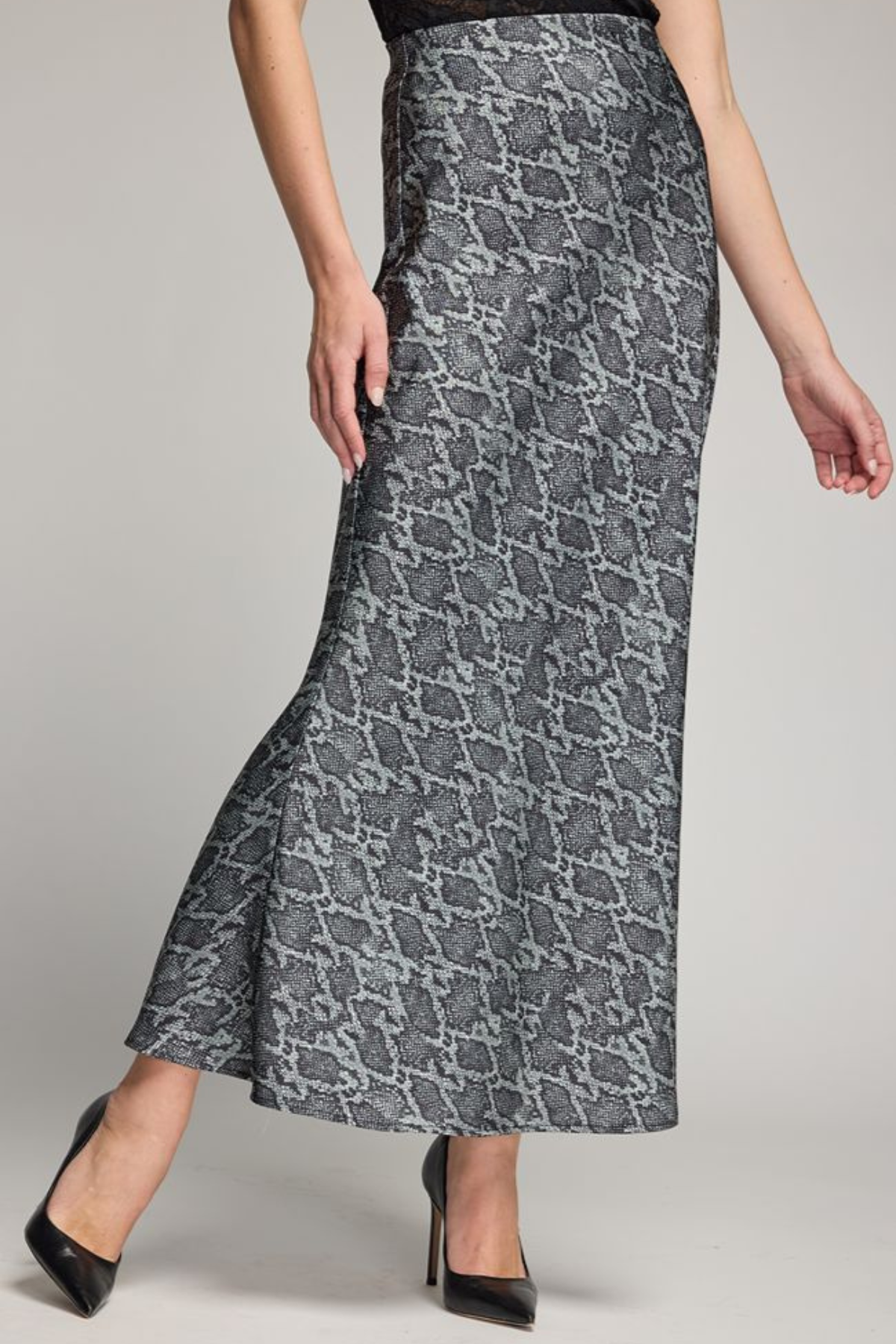 A woman modeling a high-waisted, floor-length skirt with a gray and black snakeskin pattern, paired with black heels, against a neutral studio background.