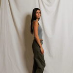 Woman wearing grey tank top standing against a plain white curtain