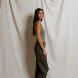 Woman wearing grey tank top standing against a plain white curtain