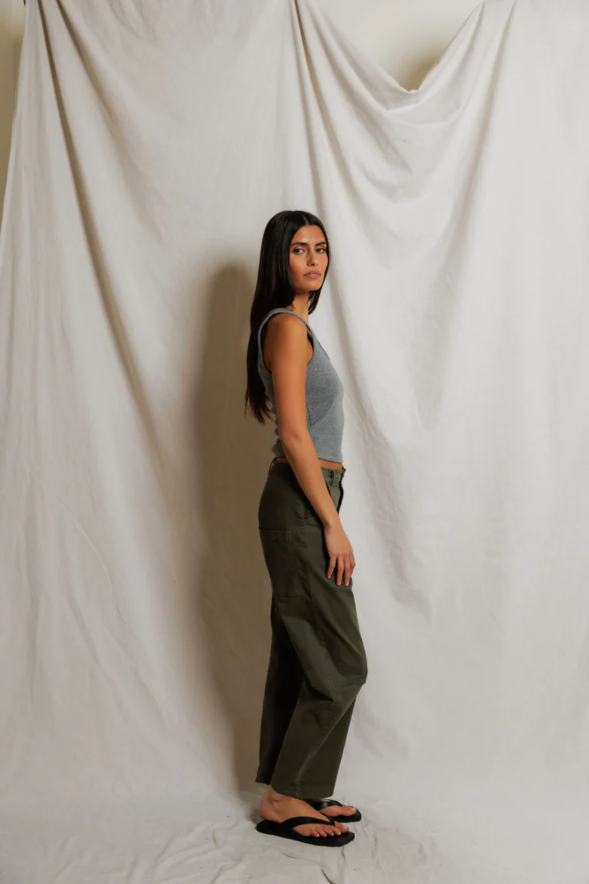 Woman wearing grey tank top standing against a plain white curtain