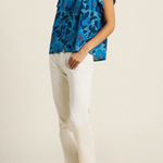 woman in blue floral blouse and white pants on tan background 
