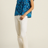 woman in blue floral blouse and white pants on tan background 