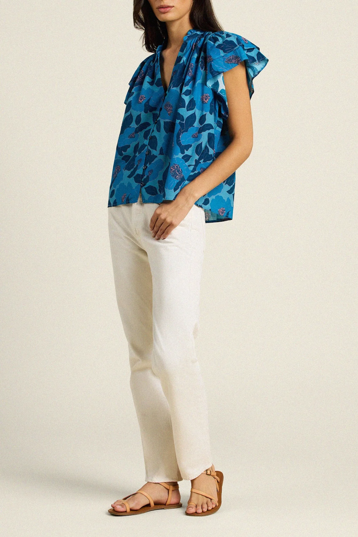 woman in blue floral blouse and white pants on tan background 