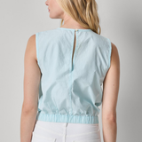 Woman wearing a light blue sleeveless top and white pants on a gray background