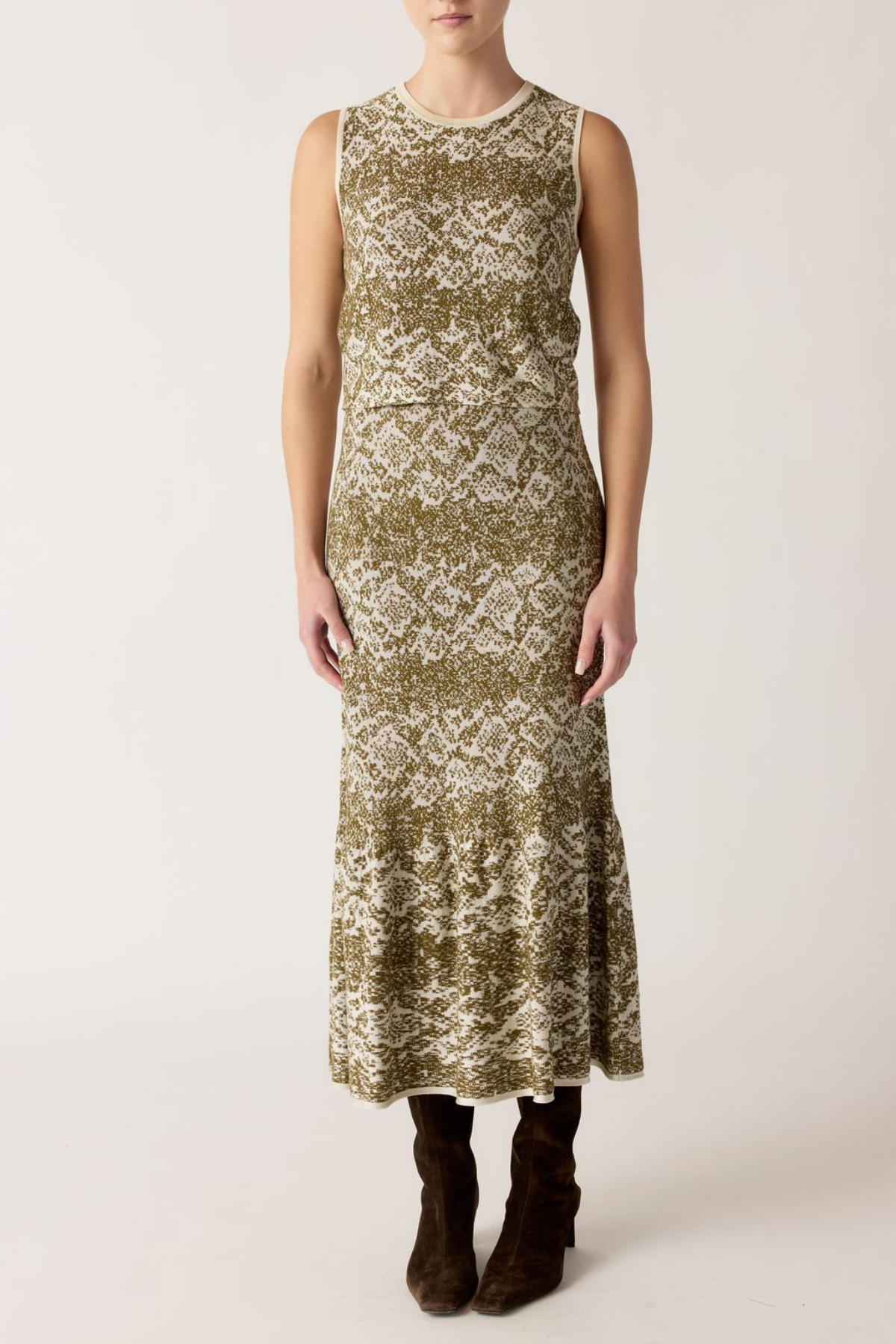 A sleeveless midi dress with a textured, abstract pattern in olive green and cream, worn by a model with dark brown ankle boots against a plain light background.