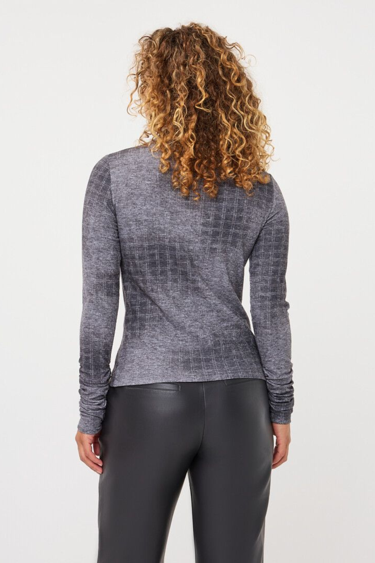 A woman with curly brown hair is shown from the back wearing a gray long-sleeve textured knit top and black leggings against a plain white background.