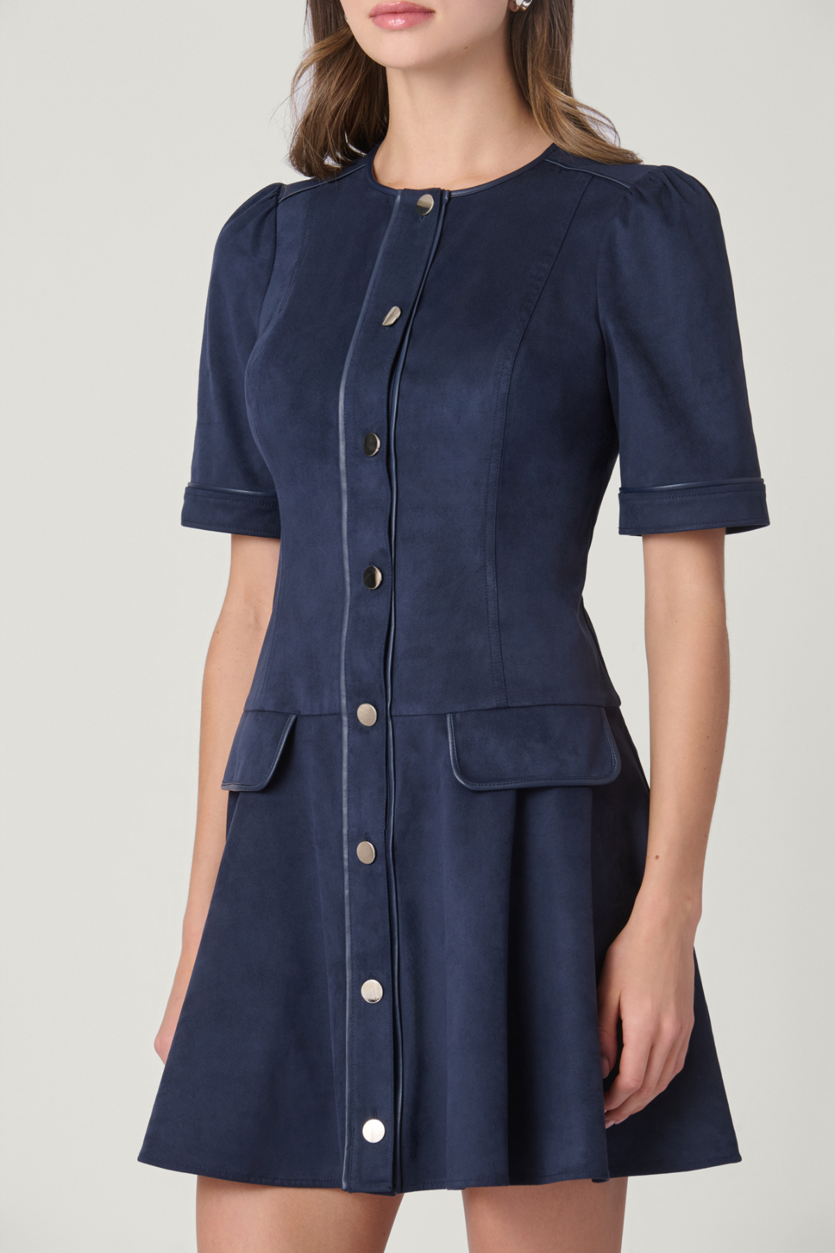 A navy blue short-sleeve button-front dress with structured shoulders and front flap pockets, shown on a model against a light gray studio background.