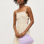 Woman holding a purple clutch bag against a plain background