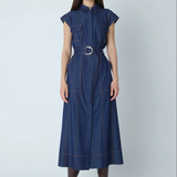 A woman modeling a dark blue denim midi dress with a matching belt and silver buckle, styled with brown leather boots against a light gray studio background.