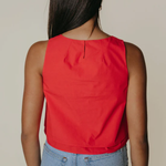 Person wearing a red sleeveless top and blue jeans on a beige background