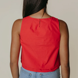 Person wearing a red sleeveless top and blue jeans on a beige background