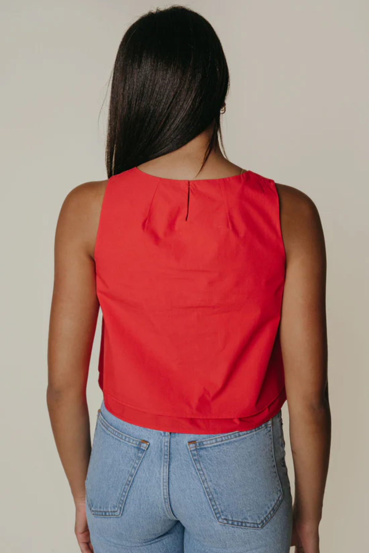 Person wearing a red sleeveless top and blue jeans on a beige background