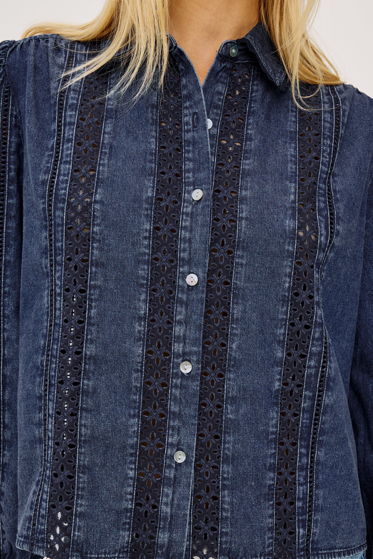 A close-up of a dark blue denim button-up shirt with vertical eyelet lace panels on the front, worn by a model whose blonde hair is visible at the collar.