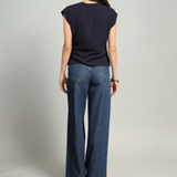 A woman shown from the back wearing a navy blue sleeveless top and wide-leg blue jeans, standing against a light gray studio background.