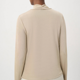A woman shown from the back wearing a light beige long-sleeve knit top with a high folded collar, paired with off-white pants, against a plain light gray studio background.