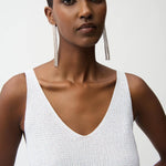 Woman wearing a white sleeveless top with long earrings on a plain background